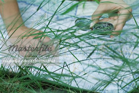 Woman pointing to map and holding compass, close-up, grass in foreground