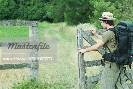 Hiker with backpack opening wooden fence