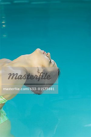 Young woman in pool, bending head backwards towards water, cropped view