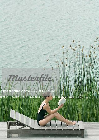 Young woman sitting on lounge chair, reading
