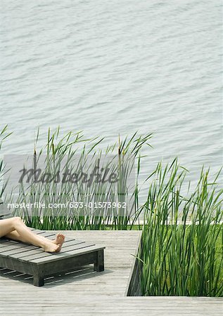 Young woman lying on lounge chair, cropped view of legs