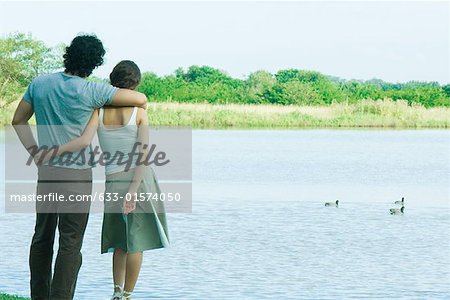Couple standing by lake, looking at view, rear view