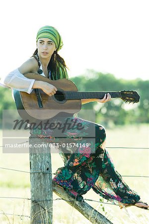 Femme jeune hippie assis sur le poteau de clôture, jouer de la guitare
