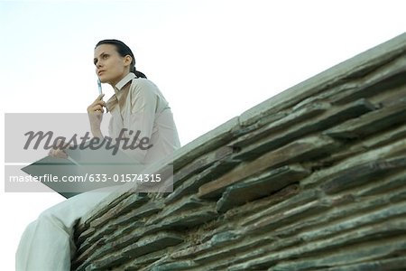 Businesswoman holding file and pen, thinking, low angle view