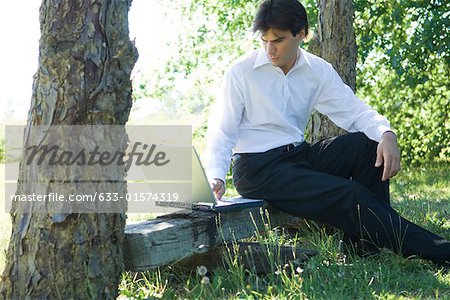 Businessman sitting on bench, under tree, using laZSop