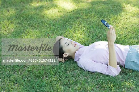 Femme couchée dans l'herbe, regardant de téléphone cellulaire