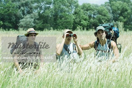Three hikers standing in field, one looking through binoculars