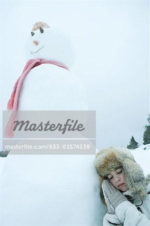 Teen girl resting head against snowman