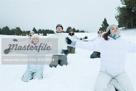 Group kneeling in snow with arms out and eyes closed