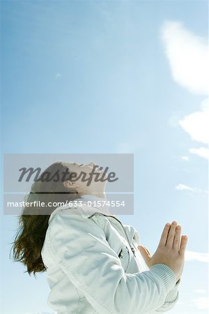 Teen girl with hands clasped, eyes closed and head back, low angle view