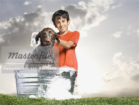 Boy bathing dog outdoors on cloudy day