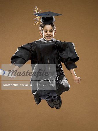 Boy graduate with mortar board and diploma leaping and smiling