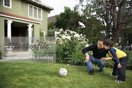 Father and Son Playing Soccer on Lawn