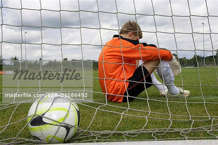 Disappointed goalkeeper sitting in goal, ball in net