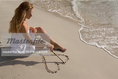 Woman Drawing Heart in Sand on Beach