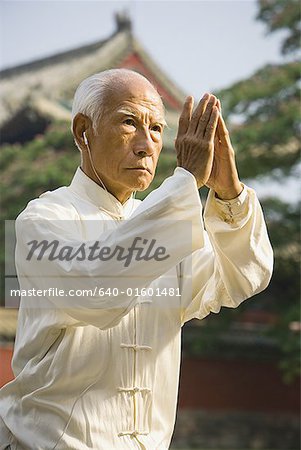 Man standing outdoors doing Kung Fu with ear buds and pagoda in background