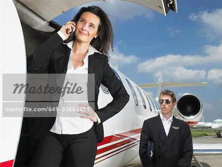 Businesswoman outside of jet in front of pilot.