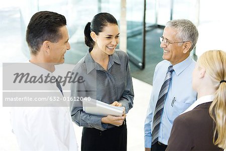 Business associates standing in lobby, smiling at each other, chatting