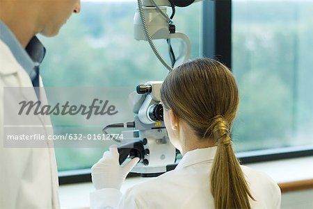 Jeune femme à l'aide de microscope, tandis que le collègue masculin montres, vue arrière