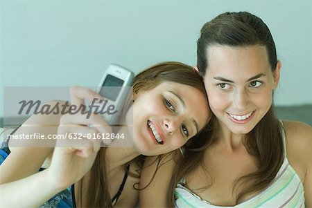 Young woman photographing self with friend, holding up cell phone