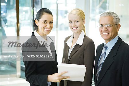 Affaires associates souriant à la caméra, une femme tenant la pile de documents