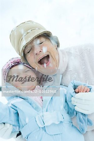 Leitende Frau und Enkelin Wange an Wange im Schnee, Lächeln, Augen, geschlossen