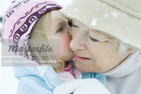 Kleinkind Mädchen küssen Großmutter auf Wange, beide gekleidet in Winterkleidung, Nahaufnahme