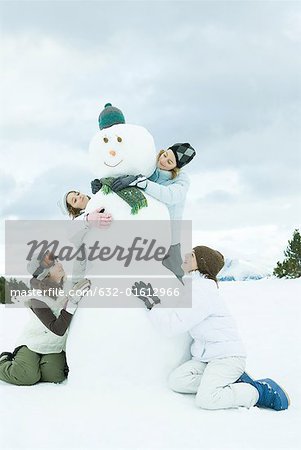 Young friends embracing snowman, smiling, full length