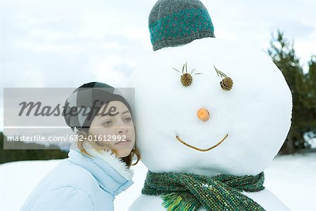 Teenage girl leaning against snowman, cheek to cheek, portrait