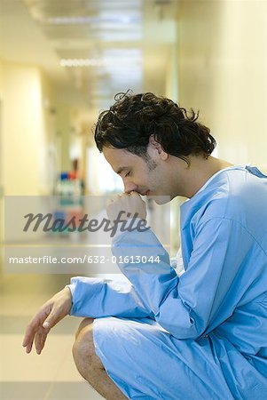 Patient masculin, accroupi dans le couloir de l'hôpital, tenant tête, regardant vers le bas