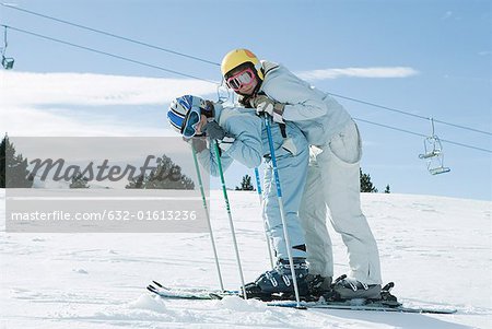 Young skiers bending over together, smiling at camera, full length portrait