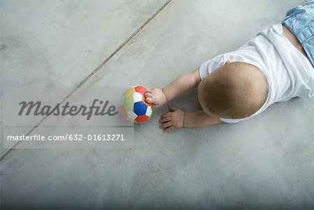 Baby crawling on floor, holding ball, view from directly above