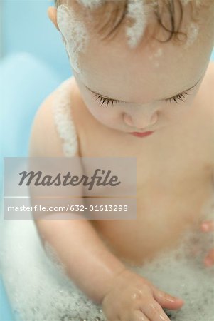 Naked baby sitting in bathtub, looking down, waist up