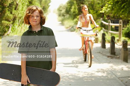 Garçon tenant Skateboard et fille vélo sur une route de campagne