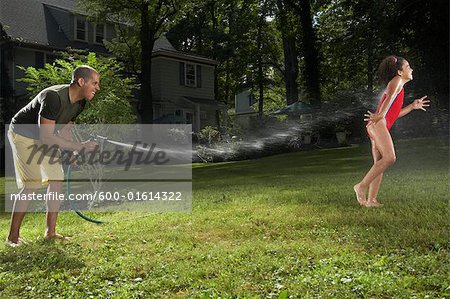 Vater und Tochter spielen mit Wasserschlauch im Garten