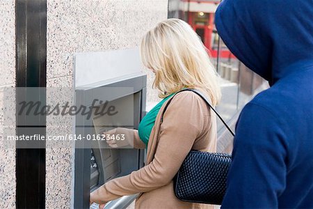 Thief looking over womans shoulder at cash machine