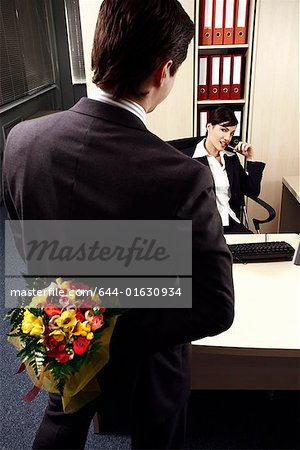 Male office worker hiding flowers for female colleague