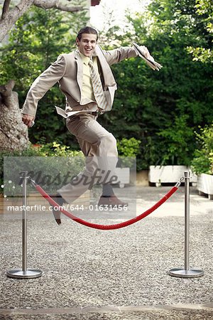 Businessman in garden jumping over barrier