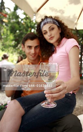 Frau sitzt auf des Mannes Schoß hält Gläser Wein