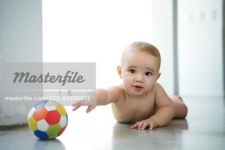 Baby lying on floor, reaching for ball and looking at camera