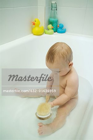 Baby taking bath, holding bath brush, full length