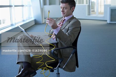 Kaufmann mit Laptop auf dem Schoß halten ein Netzwerkkabel