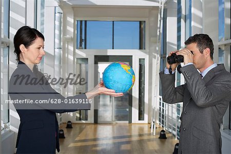 Businessman looking through field glasses to businesswoman holding a globe