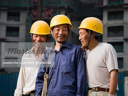 Three male construction workers with helmets outdoors smiling