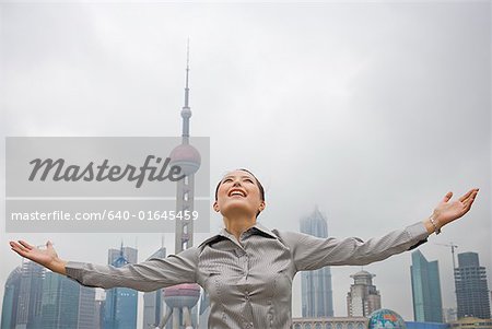 Geschäftsfrau im Freien mit Armen sich lächelnd und die Skyline der Stadt im Hintergrund