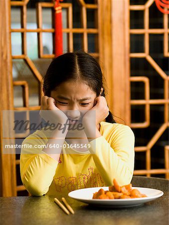 Fille assise à table, assiette de nourriture en regardant avec dégoût