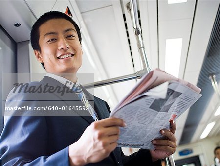 Homme d'affaires sur le métro ou le bus avec journal souriant