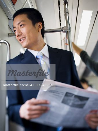 Businessman on subway or bus with newspaper smiling