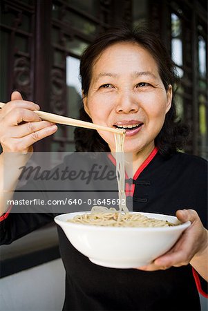 Woman with bowl of noodles and chopsticks eating