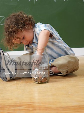 Enfant avec pot de pièces de monnaie sur le plancher dans la salle de classe